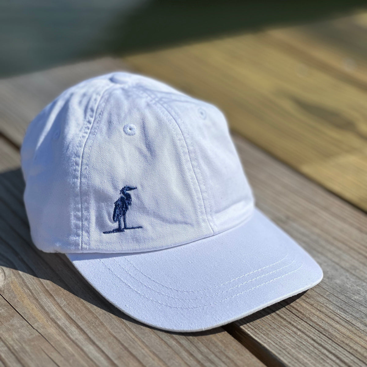 White cap with a small embroidered heron design on a wooden surface